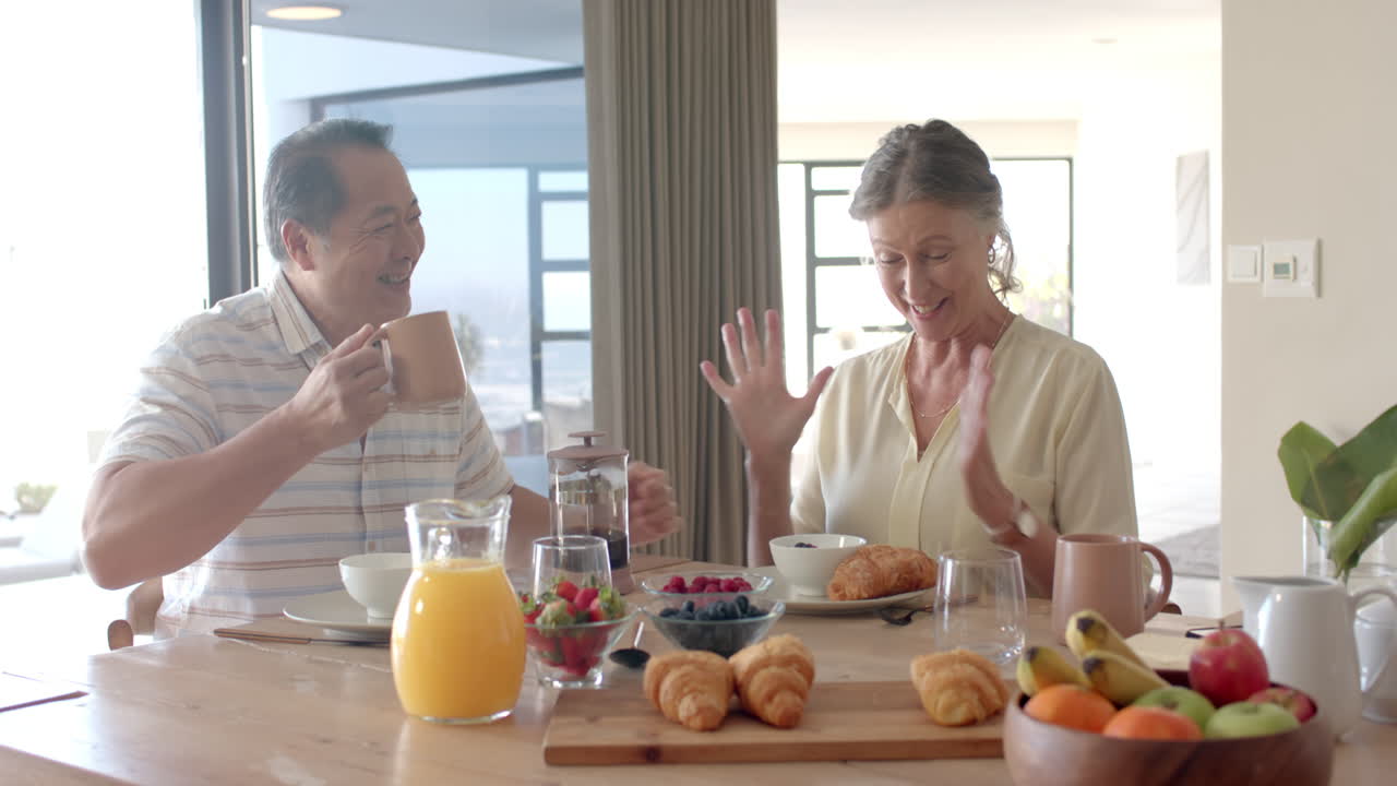 Enjoying breakfast, senior couple sitting at table with croissants and fruit