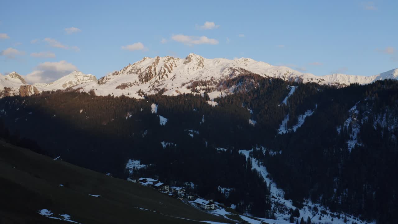Aerial drone footage of Tyrolean Alps at sunset with a night mood, featuring snowy peaks, green meadows, and white grass