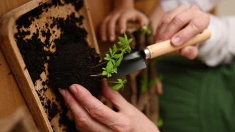 Unrecognizable-woman-with-child-standing-near-wooden-table-with-soil