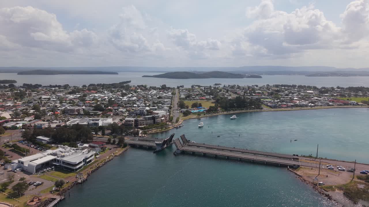 Drone pullback of boat traffic navigating open bridge in calm harbor in Swansea midday