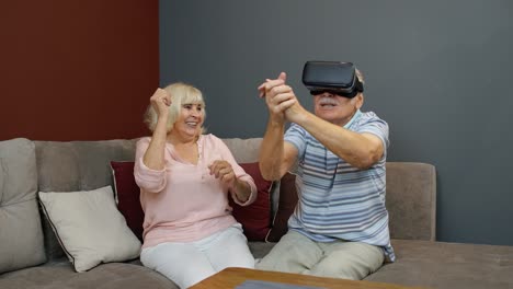 senior man playing game in virtual reality headset glasses, woman laughing with him action at home