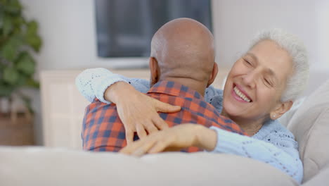 Feliz-Pareja-Birracial-Senior-Sentada-En-El-Sofá-Y-Abrazándose-En-Casa,-Cámara-Lenta