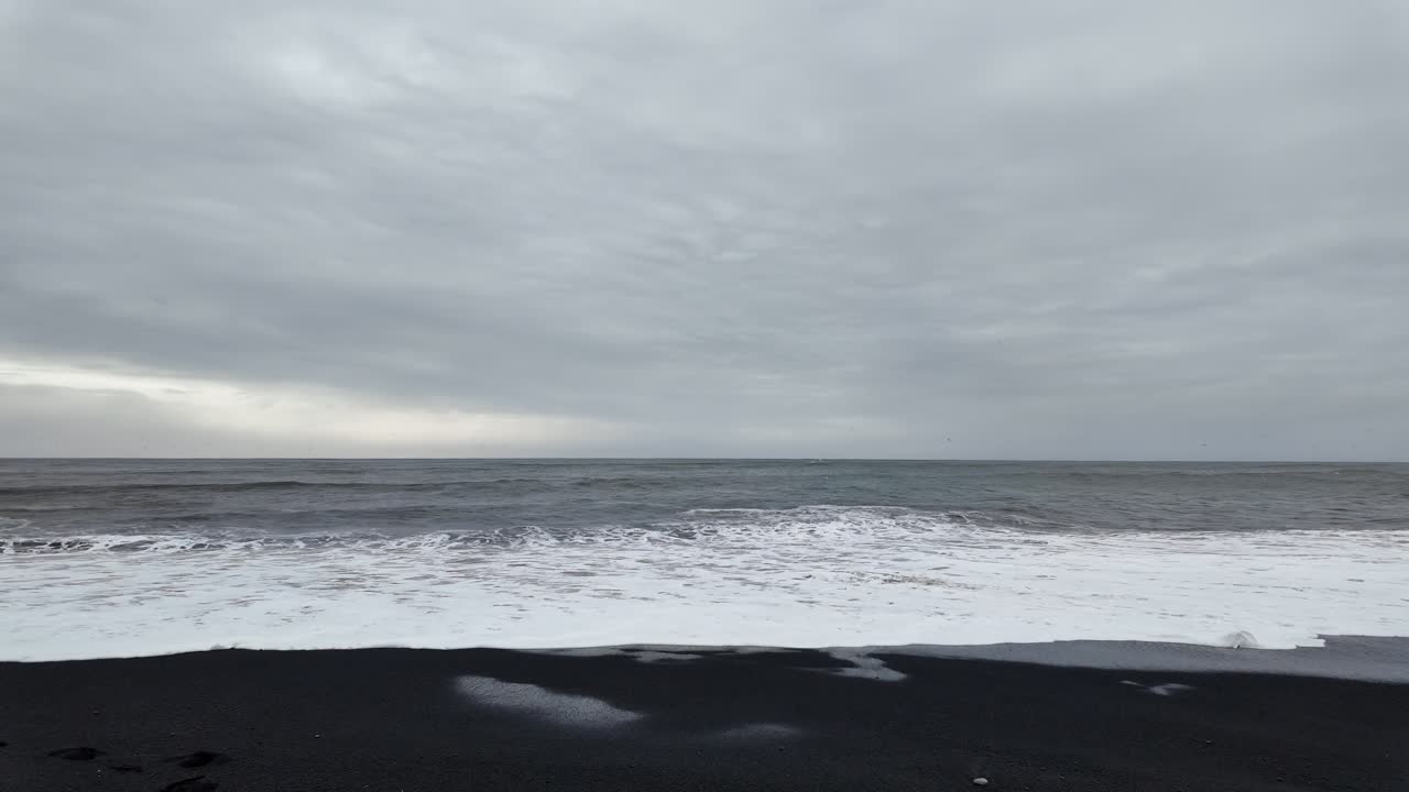 A video of Iceland's black sand beach shows dramatic waves crashing against the shore, with dark volcanic sand contrasting against the frothy white water and rugged cliffs.