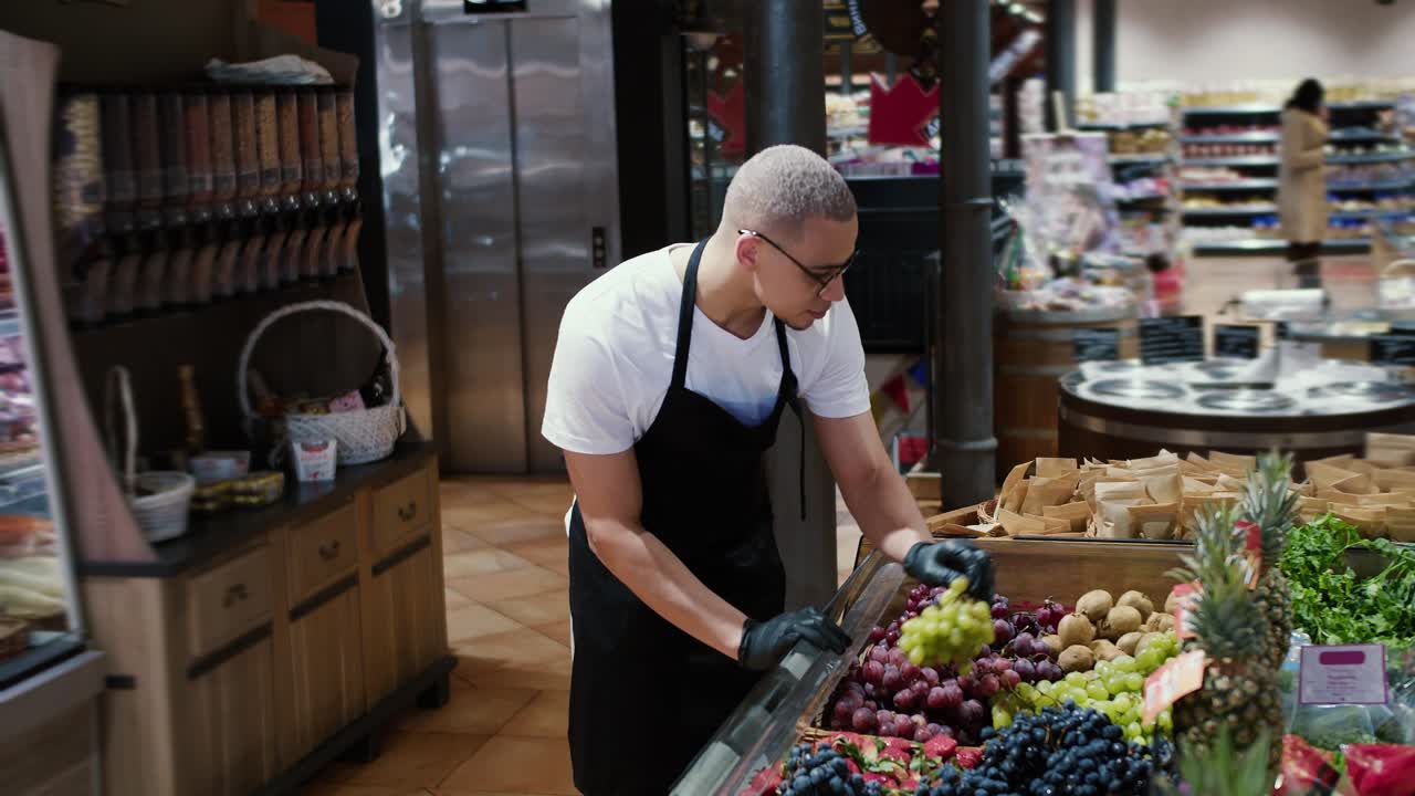 работник в черном фартуке, устраивающий свежие фрукты в разделе супермаркета