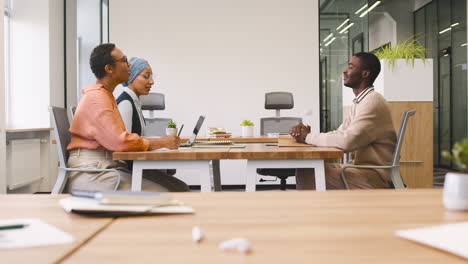 an woman and a muslim woman co workers interview a young man sitting at a table in the office 10