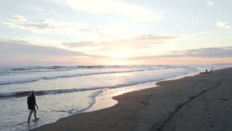 Steady-shot-over-the-ocean-surf-with-walking-tourists-in-the-distance-on-the-sandy-beach-of-playa-bandera-in-costa-rica