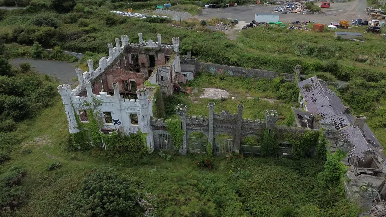Aerial view circling above Soldiers point house abandoned Holyhead coastal estate and dense woodland