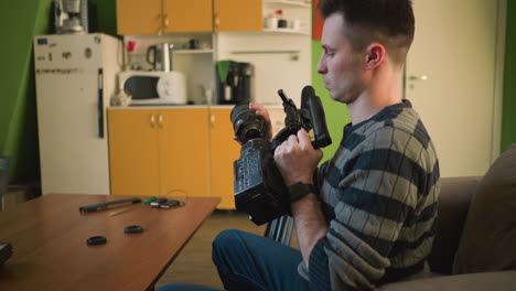 person sitting on sofa in home studio, focusing on video camera setup with tripod, preparing for filming project. workspace with coffee machine and colorful objects in background