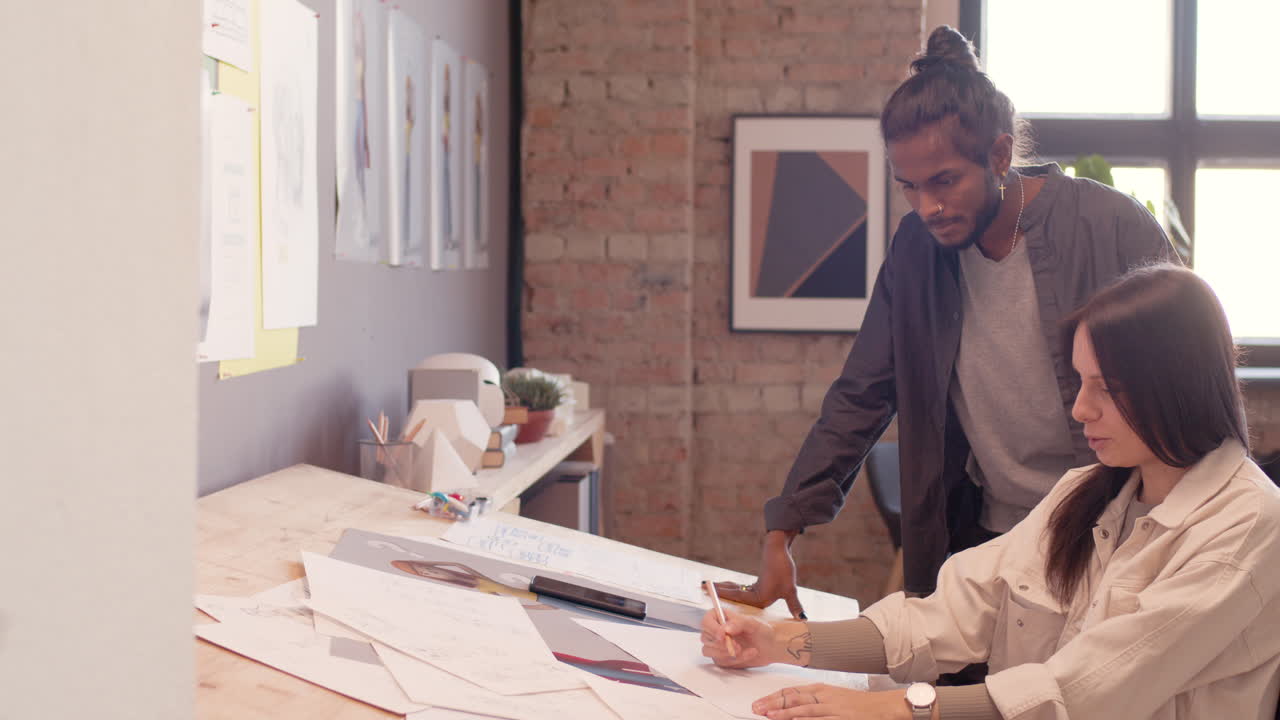 diseñadora gráfica sentada en el escritorio de dibujo y discutiendo un nuevo proyecto con su colega en un estudio de animación