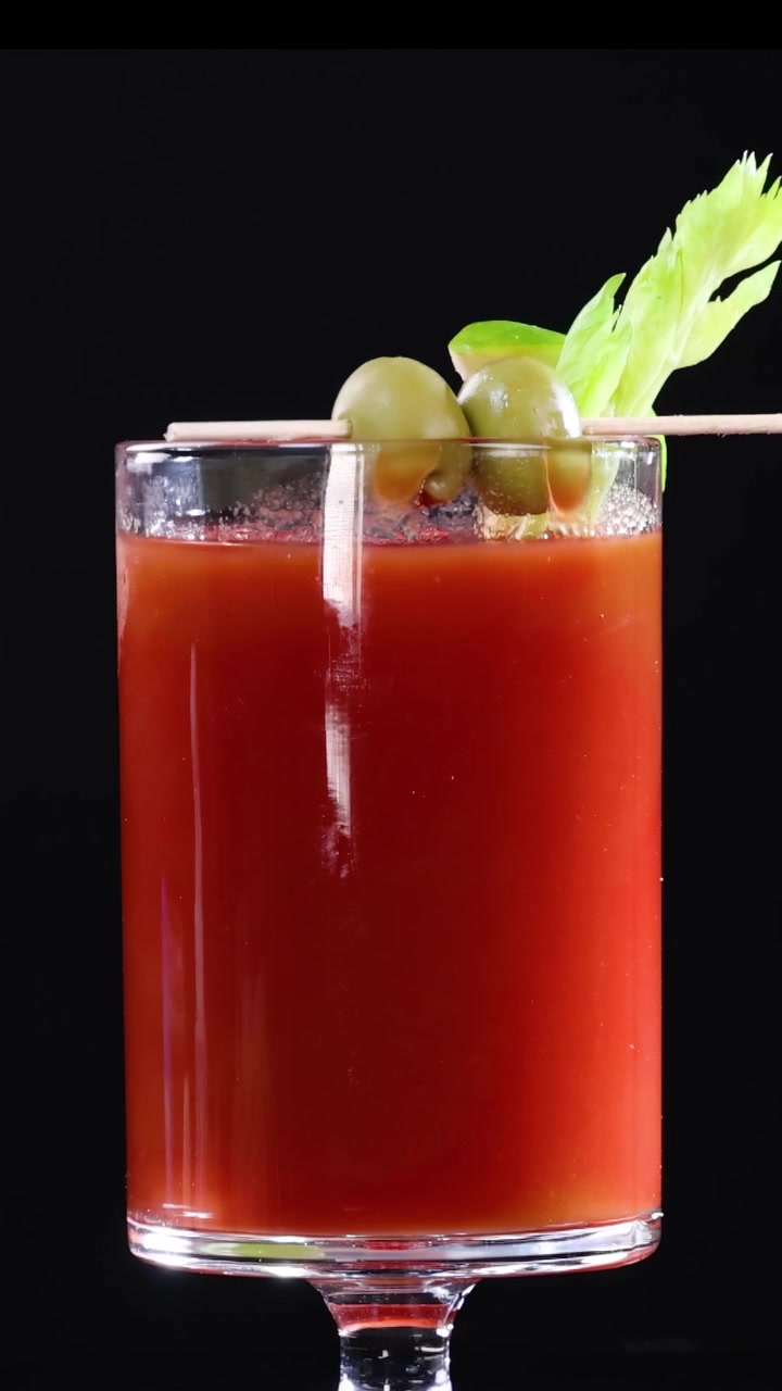 Coquetéis Bloody Mary com aipo, limão e azeitonas contra um fundo preto. A iluminação brilhante realça cores vibrantes.