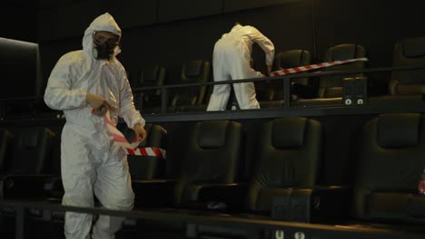 quarantine due to coronavirus pandemia - two men in protection costume stretching warning ribbons on seats