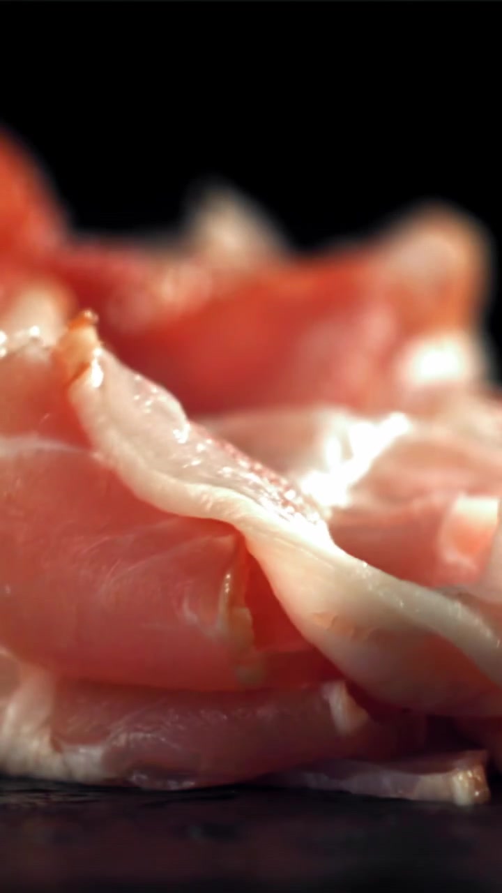 Primo piano di fette sottili di prosciutto crudo che vengono impilate