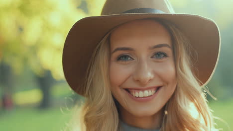 close-up view of caucasian young blonde woman wearing a hat smiling and hiding her face behind a yellow autumn leaf in the park