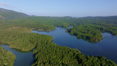 rincon dam reservoir with tropical plants on sunny day with blue sky in dominican republic. aerial backwards wide shot.