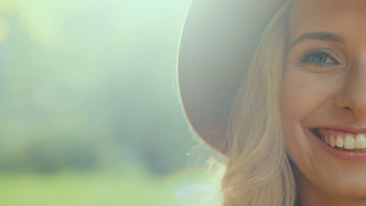 Close-up view of half face of blonde young woman wearing a hat  and smiling cheerfully to the camera in the park in autumn
