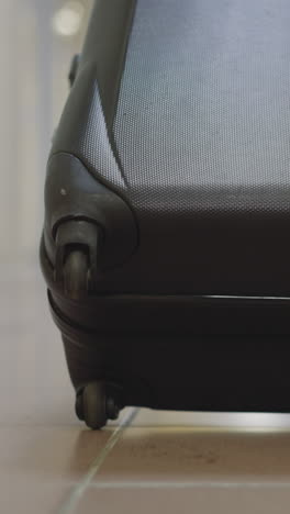 small wheels of big black suitcase with clothes spin on tile floor on blurred background. traveler takes baggage walking on hotel corridor closeup