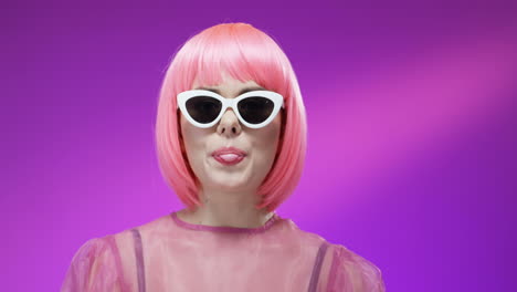 close up of stylish woman wearing a pink wig and glasses and chewing gum