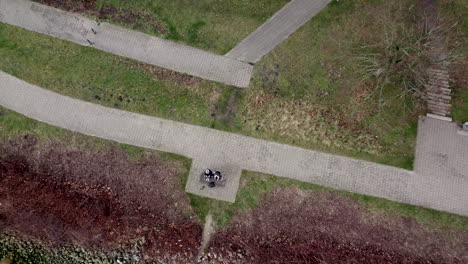 two people sitting on bench beside river in park,ascending aerial top down