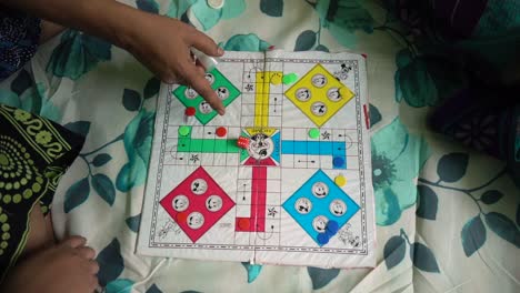 asian indian family plays ludo board game as entertainment on covid19 lockdown, man rolls the dice, top down view, slow motion shot