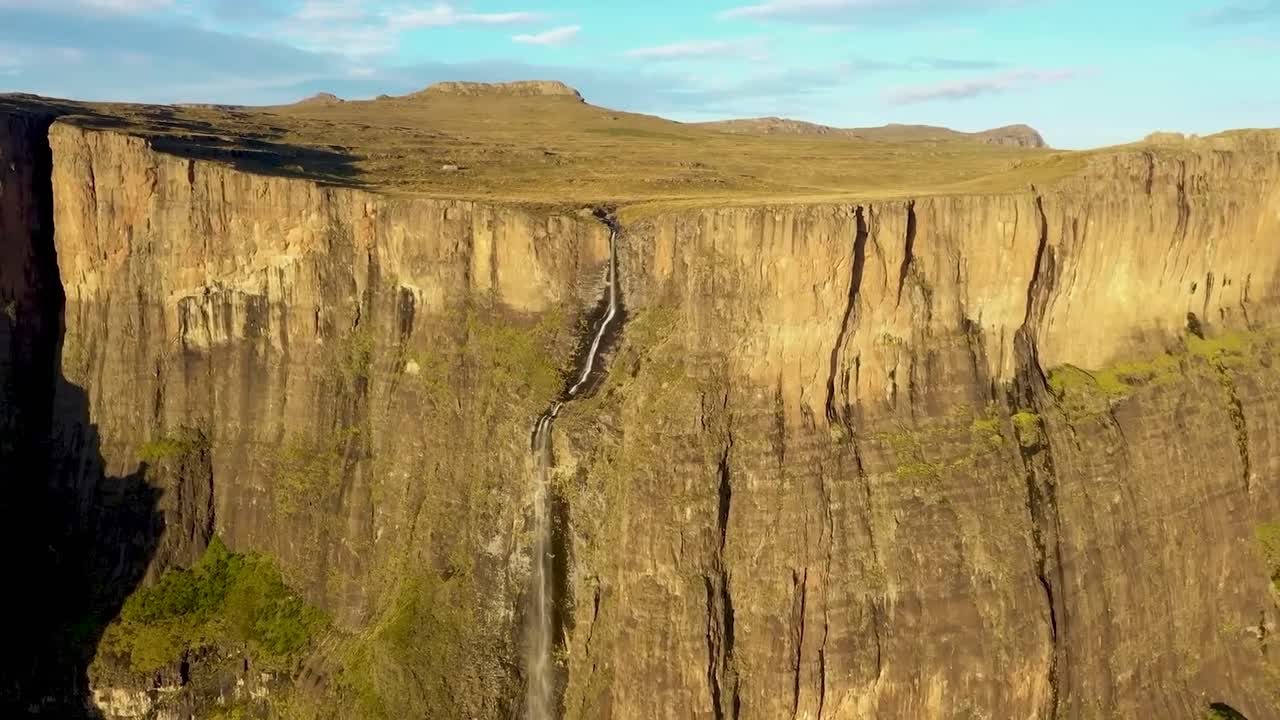 Aerial drone footage flying closer to Tugela Falls waterfall in Sauth Africa Royal Natal park during a sunny summer day. The narrow river is falling down from a very tall and steep brown cliff.