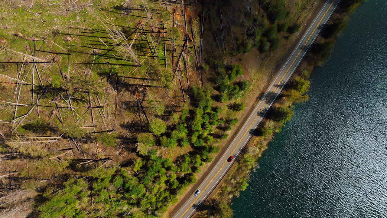 Drone footage above the highway with lonely car riding by. Mountainous area with river flowing at the foot. Top perspective.