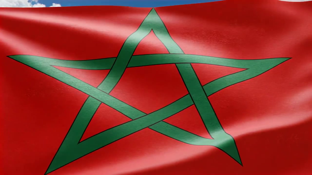 Bandiera nazionale rossa con stella verde che sventola, mostrando pieghe contro il cielo blu, mossa da una brezza costante.