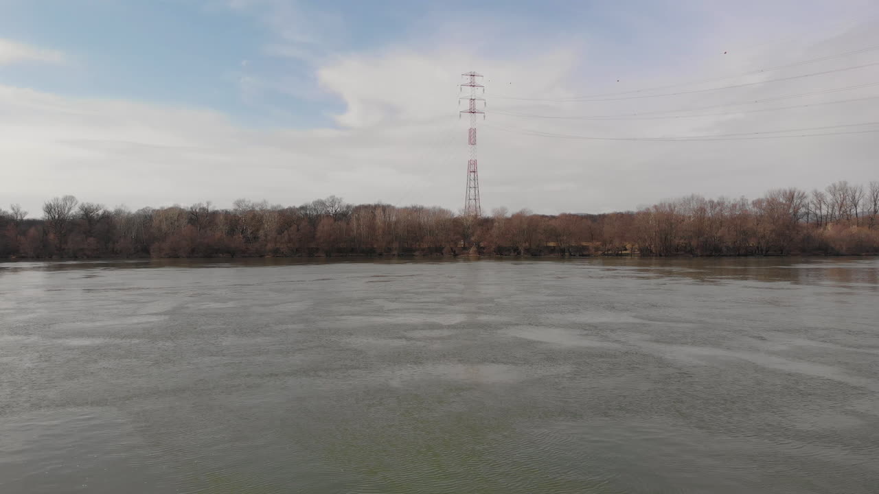 toma aérea volando sobre un río hacia una torre eléctrica y cables