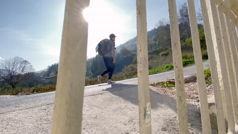 Sustainable-young-male-traveler-is-walking-up-a-hill-with-his-solar-panel-on-his-back-pack-and-barefoot-shoes