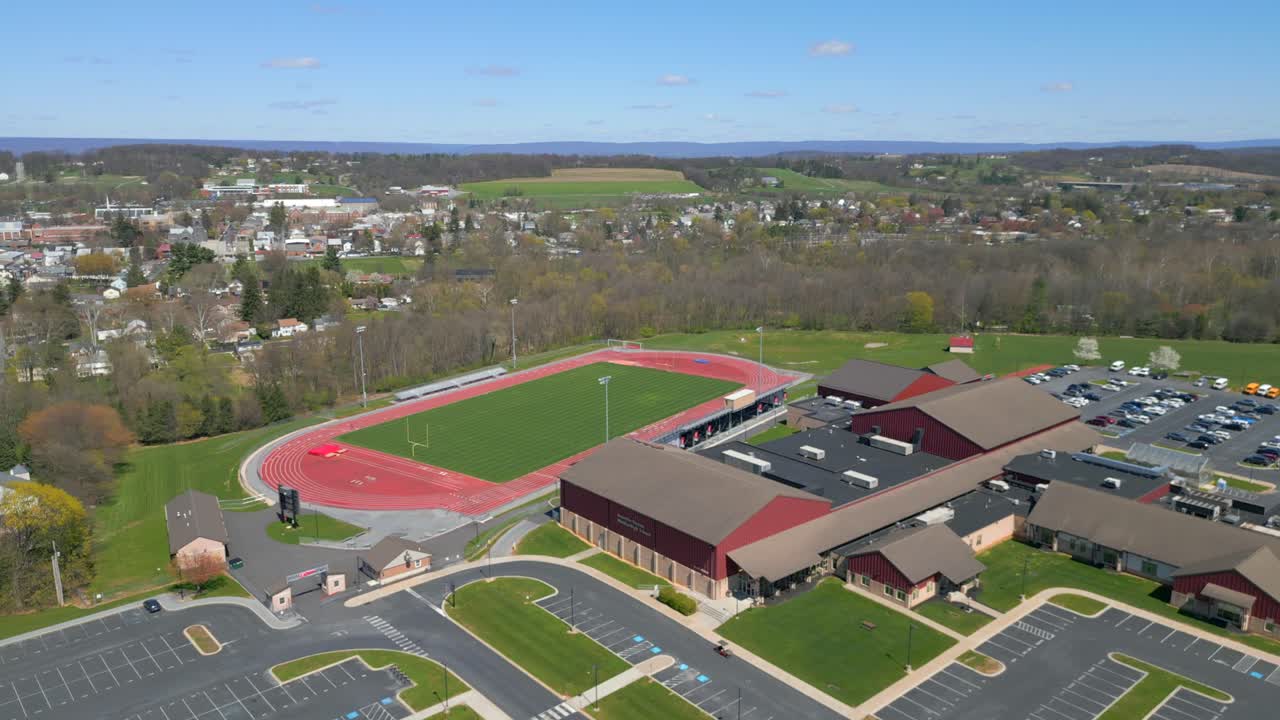 Filmato con drone dall'alto che mostra un edificio scolastico contemporaneo, un ampio parcheggio e campi sportivi verdi adiacenti durante una giornata luminosa