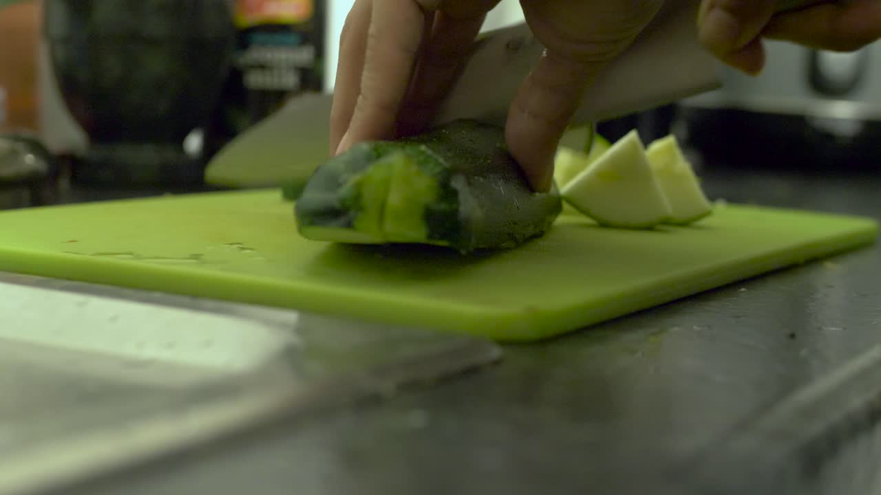 cutting a courgette with a chef's knife on a green cutting board
