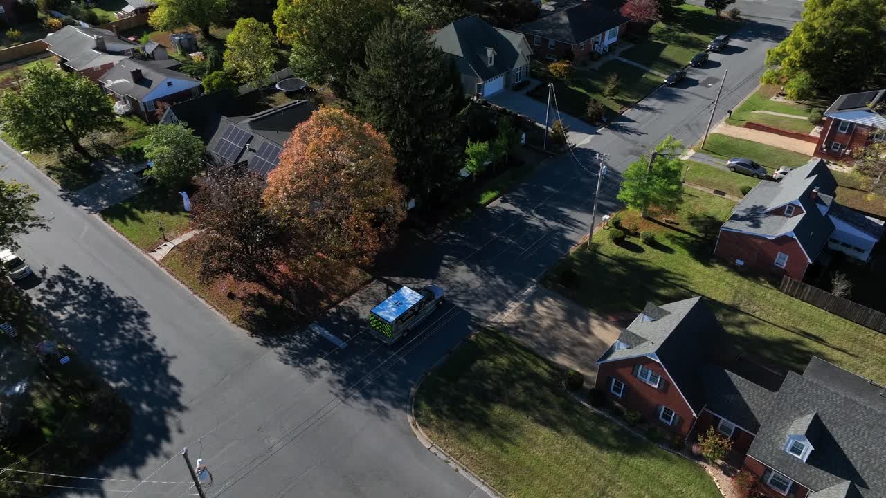 Aerial tracking shot of american ambulance car on quiet street of american neighborhood. Colored trees in fall season. Houses and homes in suburb district of city. Harrisonburg, Virginia