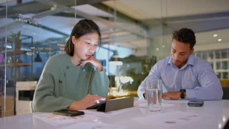 focused diverse male and female colleague discussing work and using tablet late at office