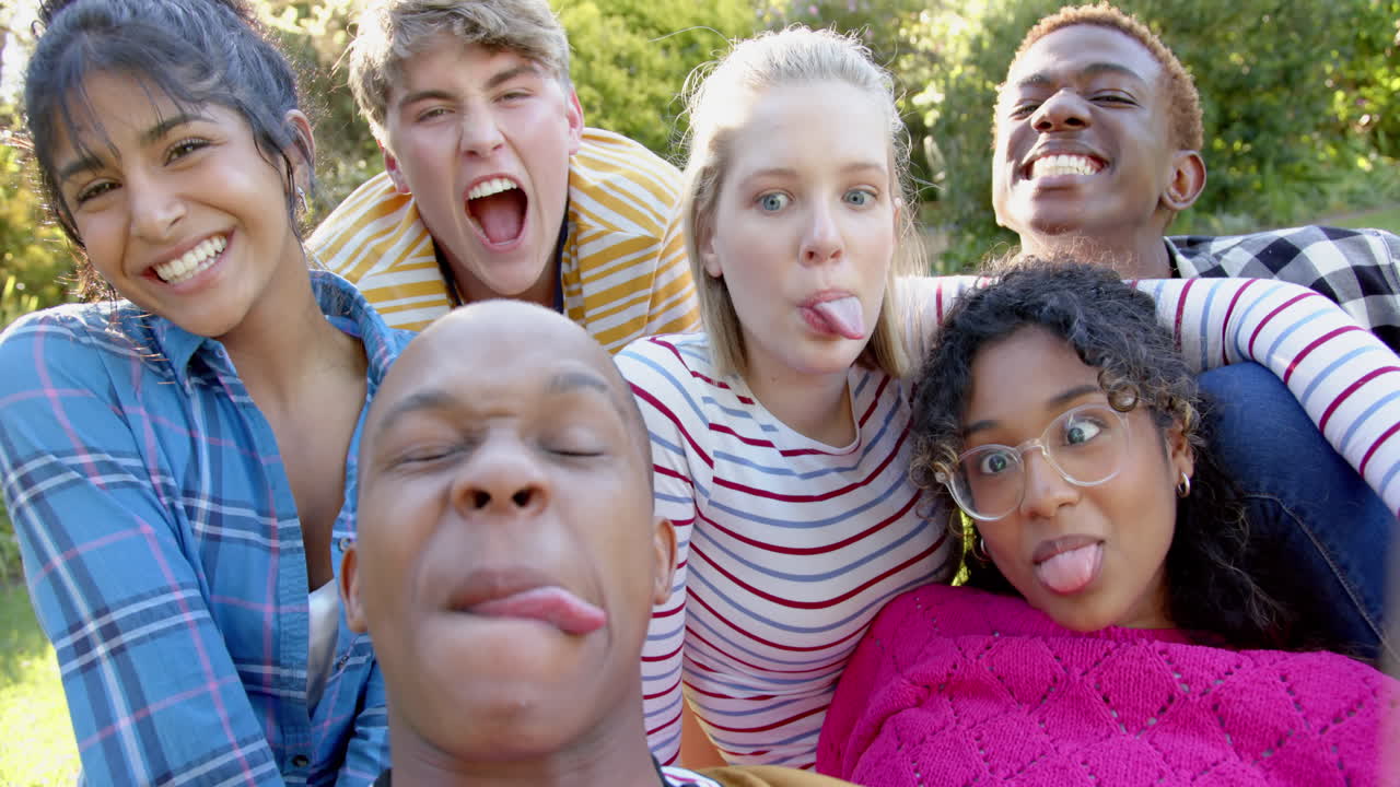 un grupo feliz y diverso de amigos adolescentes sentados en la hierba y abrazándose en un parque soleado, en cámara lenta