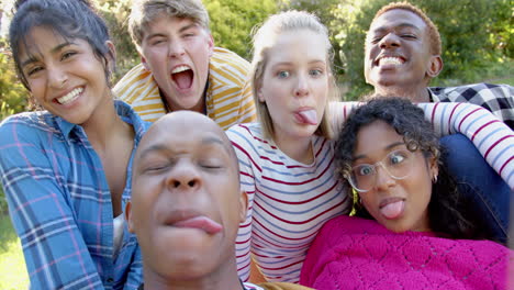 happy diverse group of teenage friends sitting on grass and embracing in sunny park, slow motion