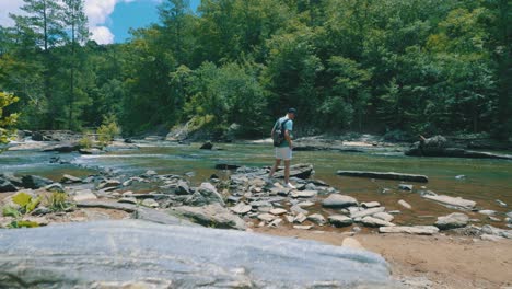 a reveal of a man walking alongside a steady flowing river, gazing at its beauty