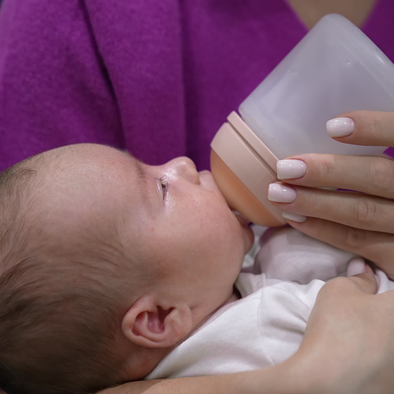 Newborn kid suckling the bottle and looking up at his mommy. Cute infant in careful mother's hands being fed. Close up