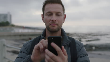 Primer-Plano-Retrato-De-Un-Hombre-Guapo-Usando-Mensajes-De-Texto-Por-Teléfono-En-La-Playa-Junto-Al-Mar