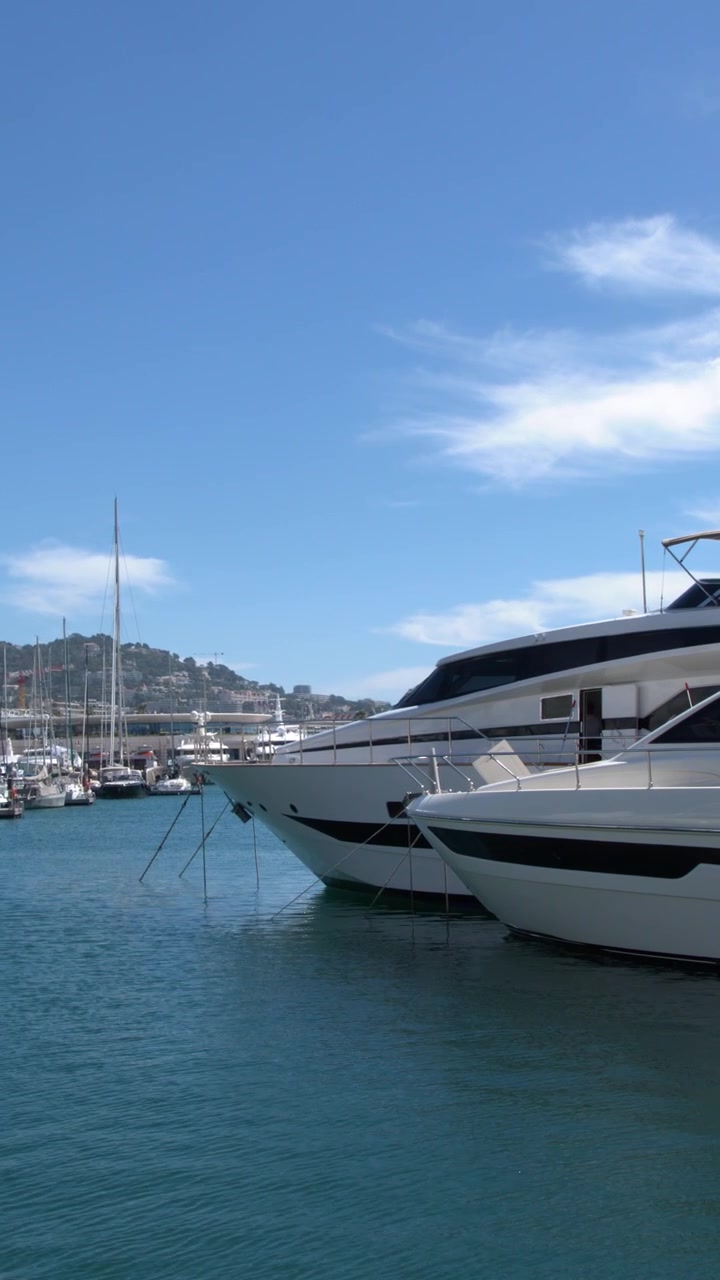 Ampia inquadratura fissa di yacht di lusso bianchi ormeggiati in acqua calma e blu sotto cieli sereni.