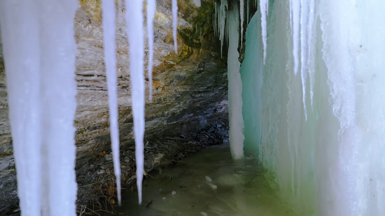 detrás de una cascada congelada con grandes carámbanos y cueva de hielo con acantilado rocoso