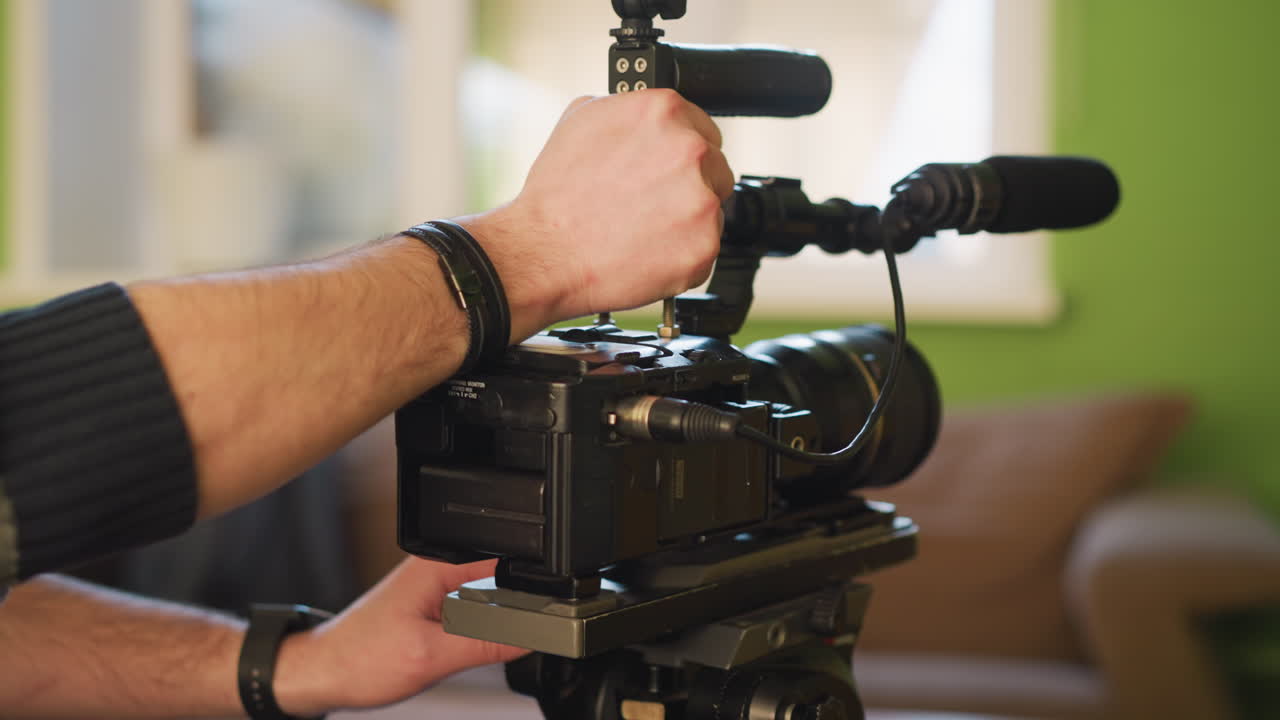 Close-up of hand positioning camera on tripod with quick release plate. Green wall in background with window light creating soft focus effect. Studio setup with bright, vibrant colors