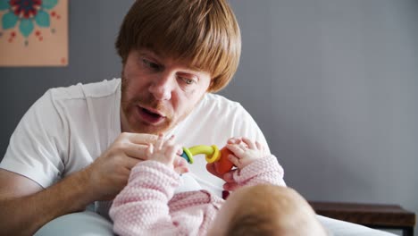 caressing dad with toy grimacing and playing with lying baby