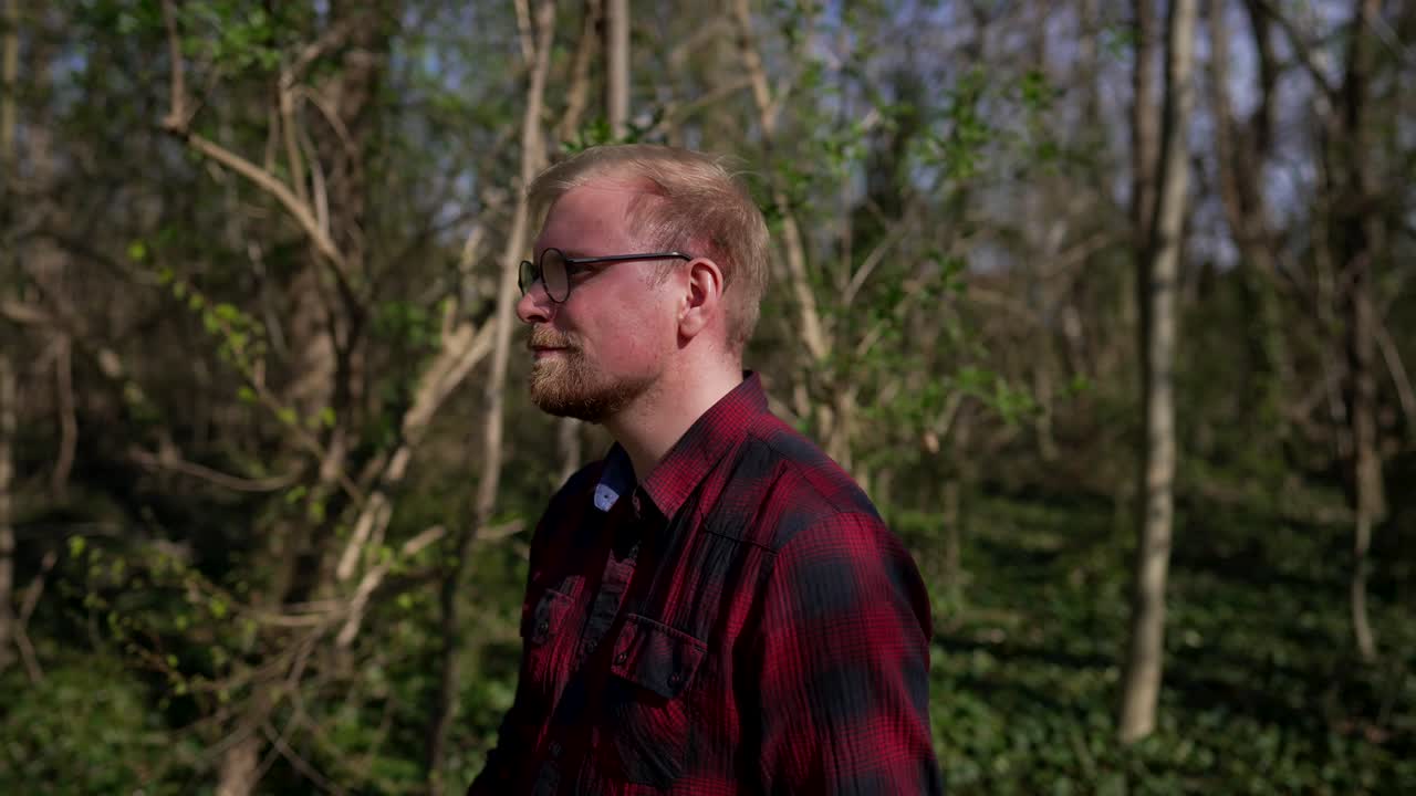 Halvnært billede af ung kaukasisk mand, der går og smiler i skoven