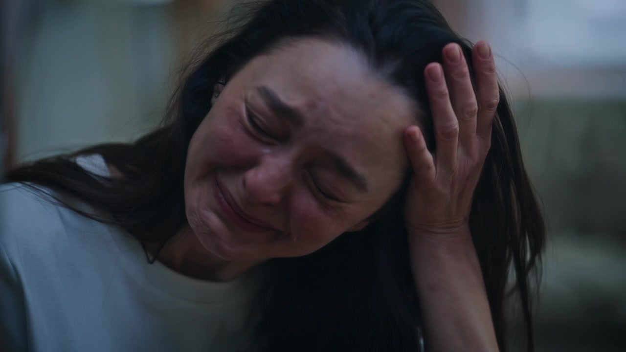 Close-up de uma mulher emotiva chorando em frente ao espelho, sentada em um apartamento à noite. Garota infeliz