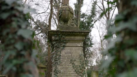 statue covered in moss and green leaves on a gravestone in a forest graveyard on a cloudy day