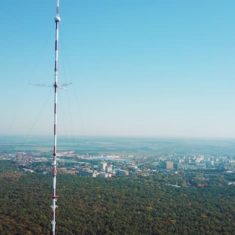 telecommunication antenna for television and radio broadcasting is located outside the city near the forest. camera motion to left