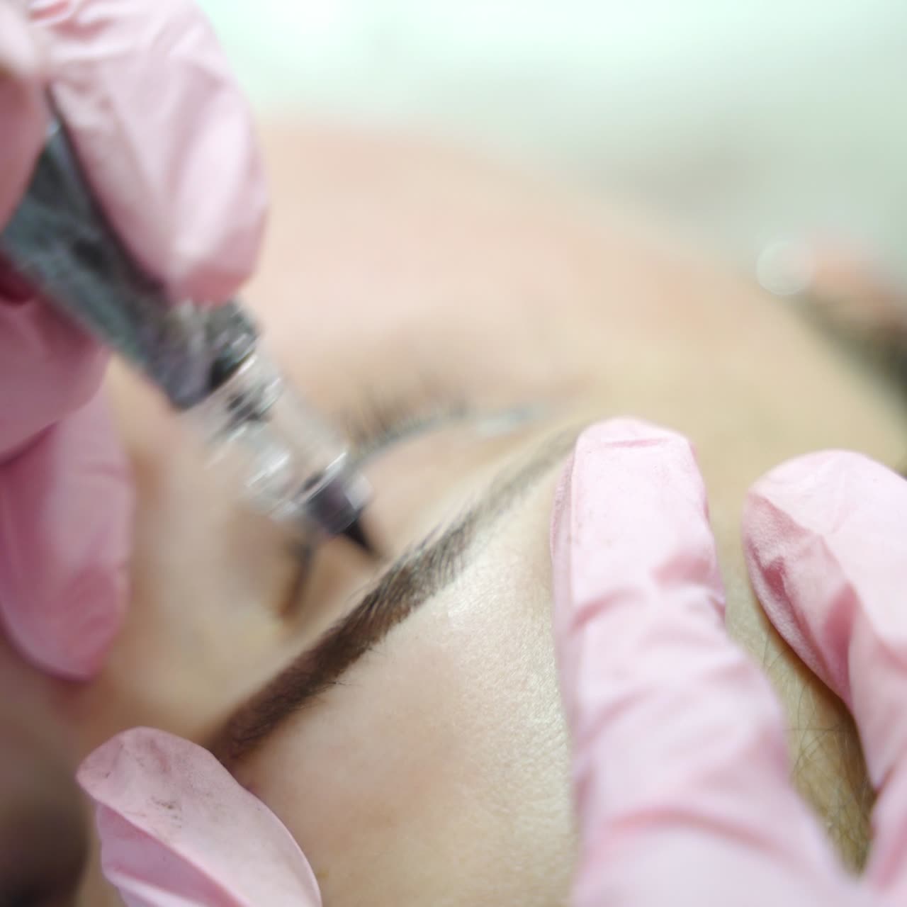 beautician is drawing the shape of eyebrows with needle for a woman in a beauty salon. Professional equipment for permanent makeup. Modern cosmetology. Blurred background
