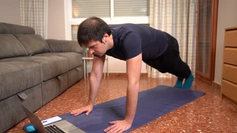 Man-doing-planks-with-computer-during-online-sport-class