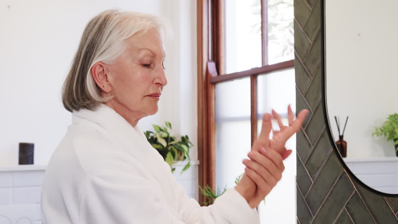 Senior woman applying lotion at home, enjoying peaceful self-care routine