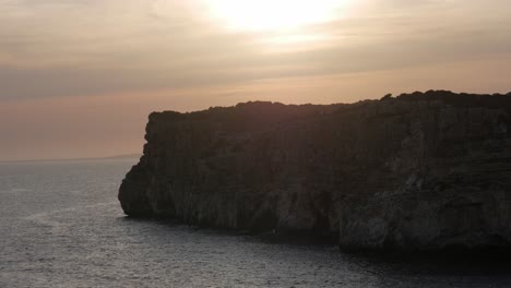 rocky coastal cliff at cova d'en xoroi, menorca, glowing under a warm sunset sky