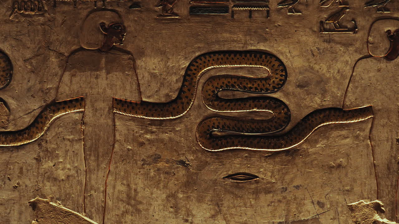 Close-up of a hieroglyphic scene in the Tomb of the Kings, showing figures holding a long snake surrounded by ancient symbols. Historic Egyptian art with religious, cultural, and mythological meaning